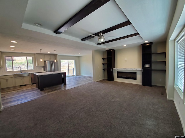 unfurnished living room with sink, beam ceiling, ceiling fan, and hardwood / wood-style floors