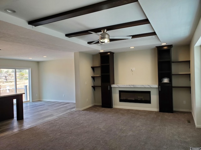 unfurnished living room featuring ceiling fan, carpet, beamed ceiling, and a fireplace