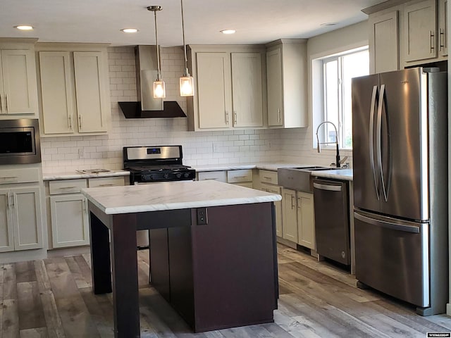 kitchen with wall chimney range hood, decorative backsplash, light wood-type flooring, pendant lighting, and appliances with stainless steel finishes