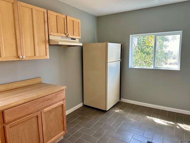 kitchen featuring white fridge, light brown cabinetry, and dark tile patterned floors