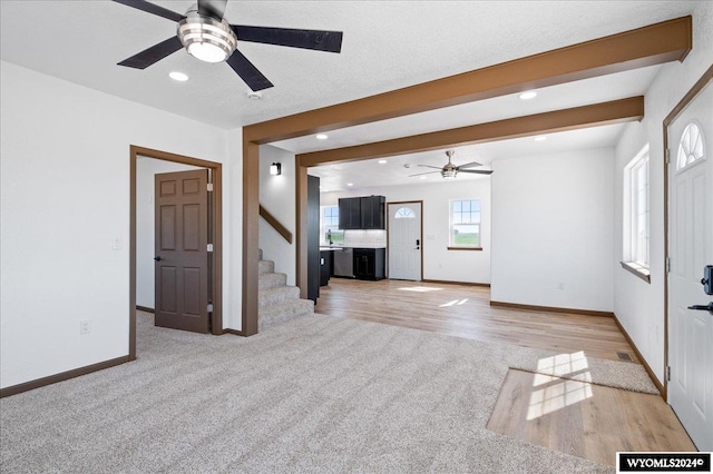 unfurnished living room with ceiling fan, light carpet, and beamed ceiling