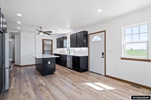 kitchen with stainless steel dishwasher, tasteful backsplash, light wood-type flooring, a kitchen island, and ceiling fan