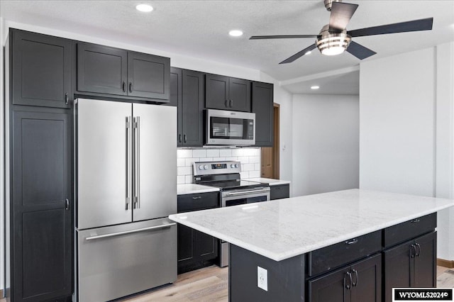 kitchen with light stone counters, decorative backsplash, light hardwood / wood-style floors, ceiling fan, and stainless steel appliances