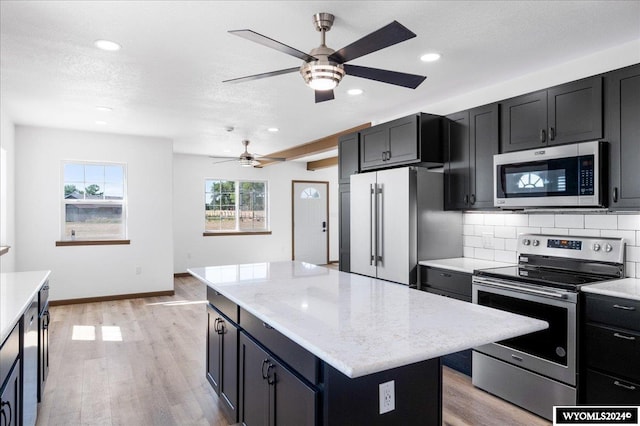 kitchen with ceiling fan, light hardwood / wood-style flooring, a kitchen island, tasteful backsplash, and stainless steel appliances