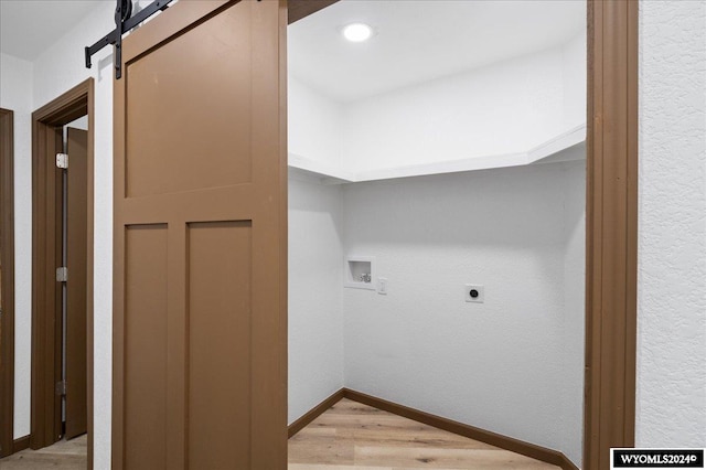 clothes washing area featuring washer hookup, hookup for an electric dryer, light wood-type flooring, and a barn door