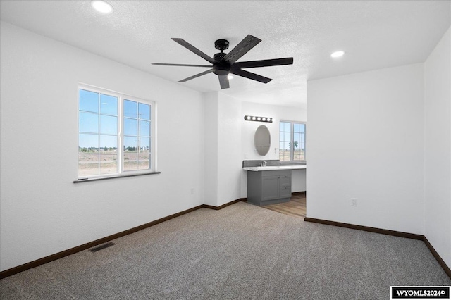 unfurnished bedroom featuring ceiling fan, ensuite bath, light colored carpet, and multiple windows