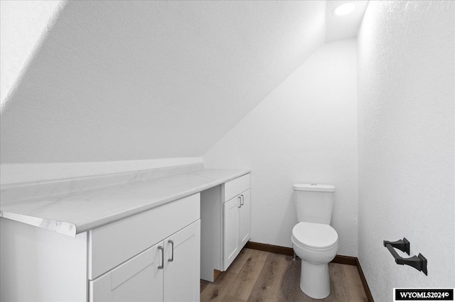 bathroom featuring vaulted ceiling, toilet, vanity, and wood-type flooring