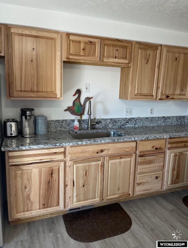 kitchen with sink, dark stone counters, a textured ceiling, and wood-type flooring