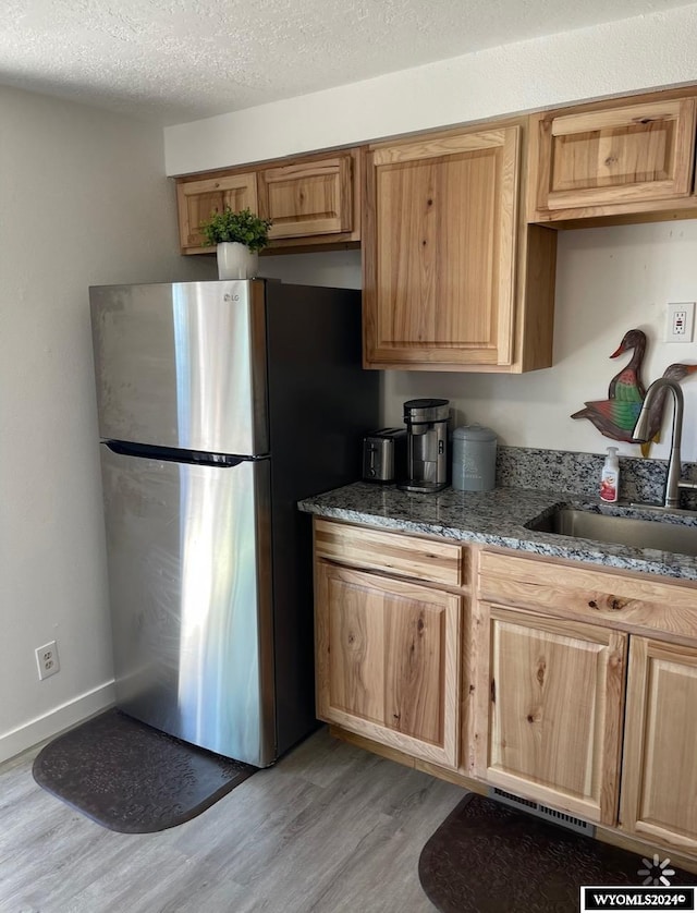 kitchen featuring light hardwood / wood-style flooring, stone counters, sink, a textured ceiling, and stainless steel fridge