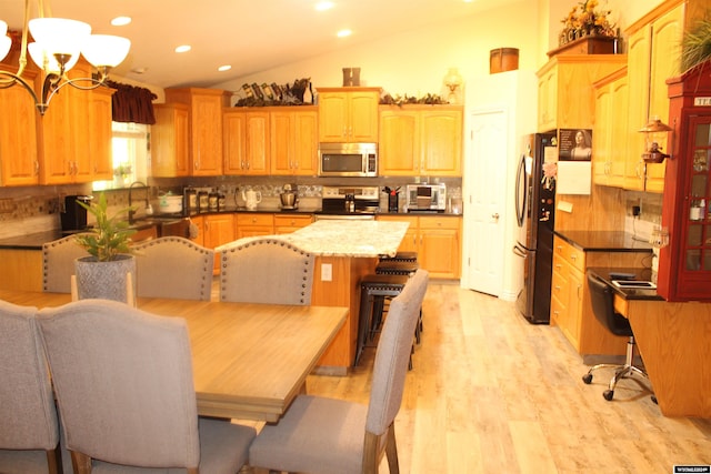 kitchen with tasteful backsplash, vaulted ceiling, an inviting chandelier, and stainless steel appliances