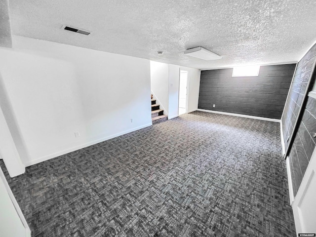 interior space with carpet floors, visible vents, stairway, wooden walls, and a textured ceiling