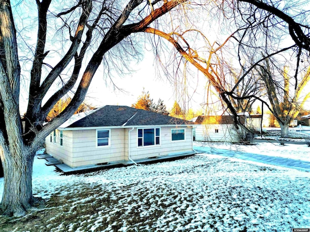 snow covered rear of property featuring roof with shingles