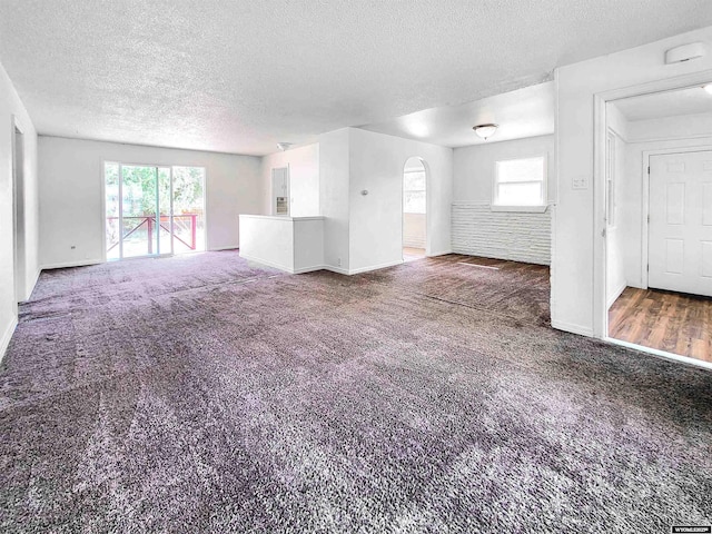 unfurnished living room with carpet floors, arched walkways, a textured ceiling, and baseboards