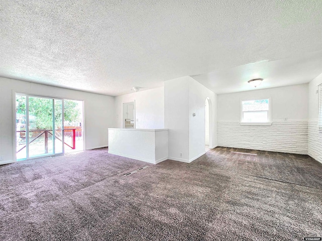 empty room featuring a textured ceiling, carpet floors, and arched walkways