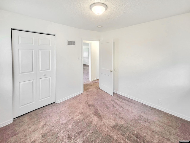 unfurnished bedroom with carpet floors, a closet, visible vents, a textured ceiling, and baseboards