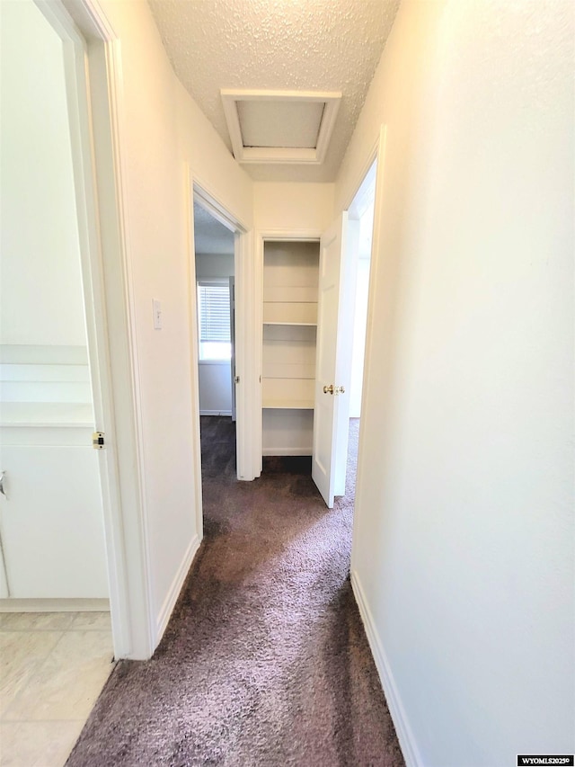 hall featuring a textured ceiling, carpet floors, attic access, and baseboards