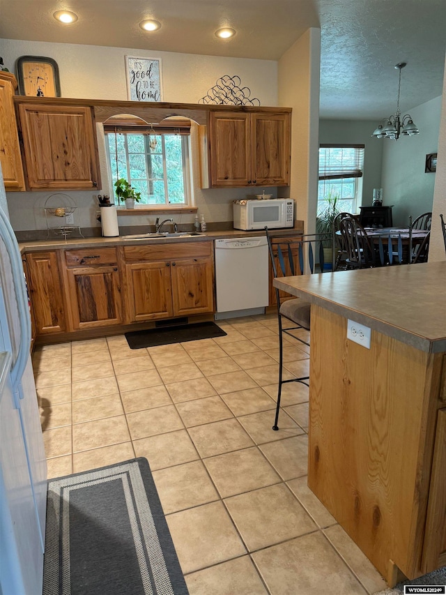 kitchen with light tile patterned flooring, a kitchen breakfast bar, white appliances, a chandelier, and pendant lighting