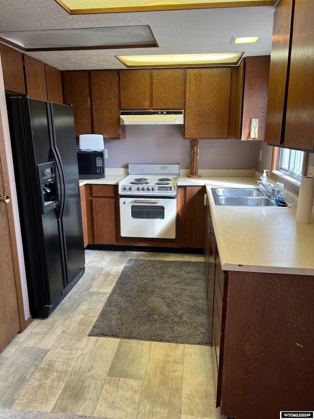 kitchen featuring white electric stove, light countertops, a sink, under cabinet range hood, and black fridge