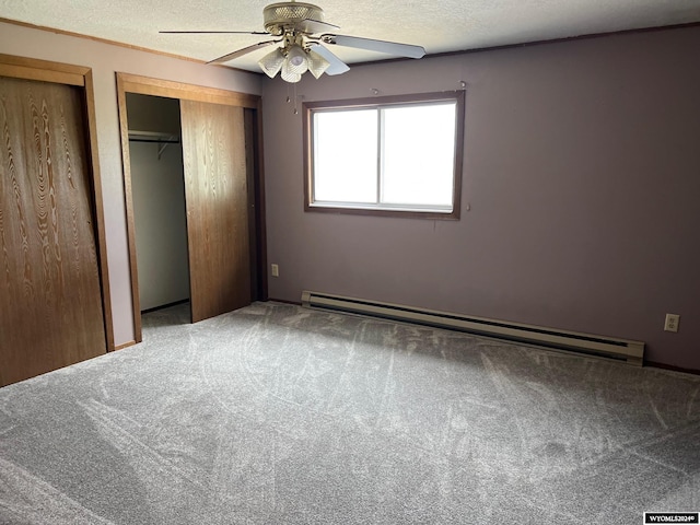 unfurnished bedroom with carpet flooring, a textured ceiling, baseboard heating, and two closets