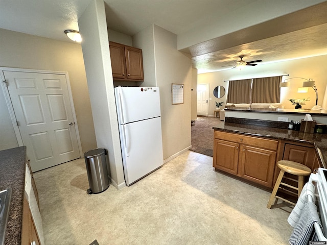 kitchen with dark stone countertops, white fridge, stove, ceiling fan, and light colored carpet