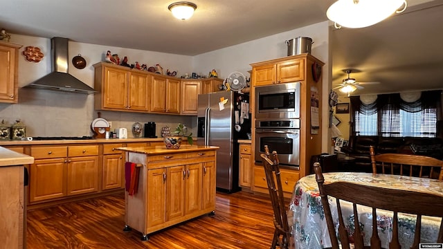 kitchen with ceiling fan, wall chimney range hood, appliances with stainless steel finishes, and dark hardwood / wood-style flooring