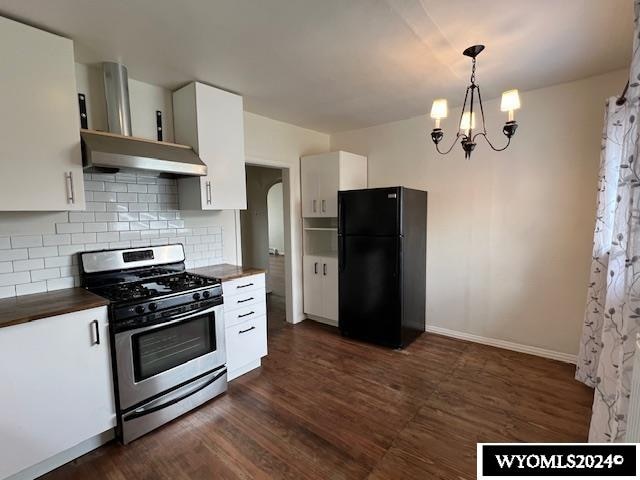 kitchen featuring an inviting chandelier, stainless steel gas stove, black refrigerator, dark hardwood / wood-style floors, and wall chimney exhaust hood