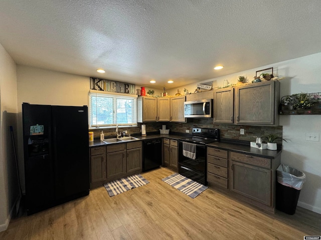 kitchen with a textured ceiling, backsplash, black appliances, sink, and light hardwood / wood-style floors