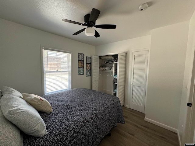 bedroom with a textured ceiling, ceiling fan, dark hardwood / wood-style floors, and two closets