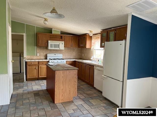 kitchen featuring a textured ceiling, a kitchen island, washer and dryer, and white appliances