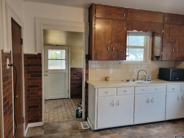 kitchen with white cabinetry, brick wall, and sink