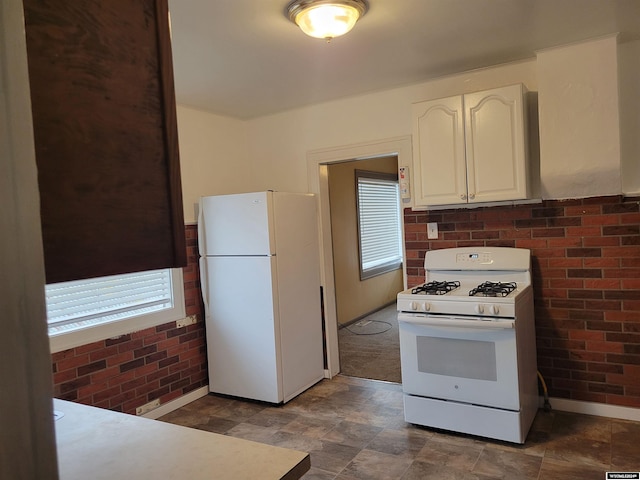 kitchen with brick wall, white cabinetry, and white appliances