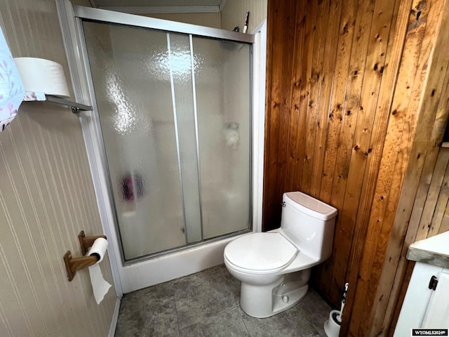 bathroom with tile patterned flooring, a shower with door, wooden walls, toilet, and vanity