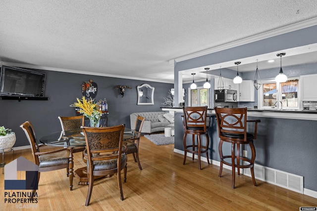 dining room with a textured ceiling, light wood-type flooring, ornamental molding, and sink