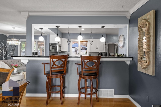 kitchen with kitchen peninsula, ornamental molding, a breakfast bar, pendant lighting, and white cabinets