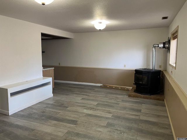 unfurnished room featuring a textured ceiling, dark hardwood / wood-style floors, and a wood stove