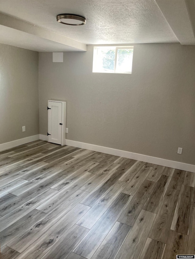 basement featuring baseboards, a textured ceiling, and wood finished floors