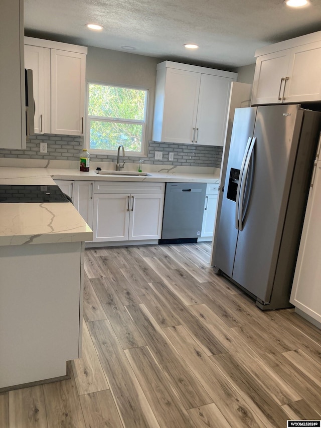 kitchen with white cabinets, light stone countertops, stainless steel appliances, light wood-type flooring, and sink