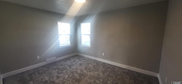 spare room with visible vents, baseboards, and dark carpet