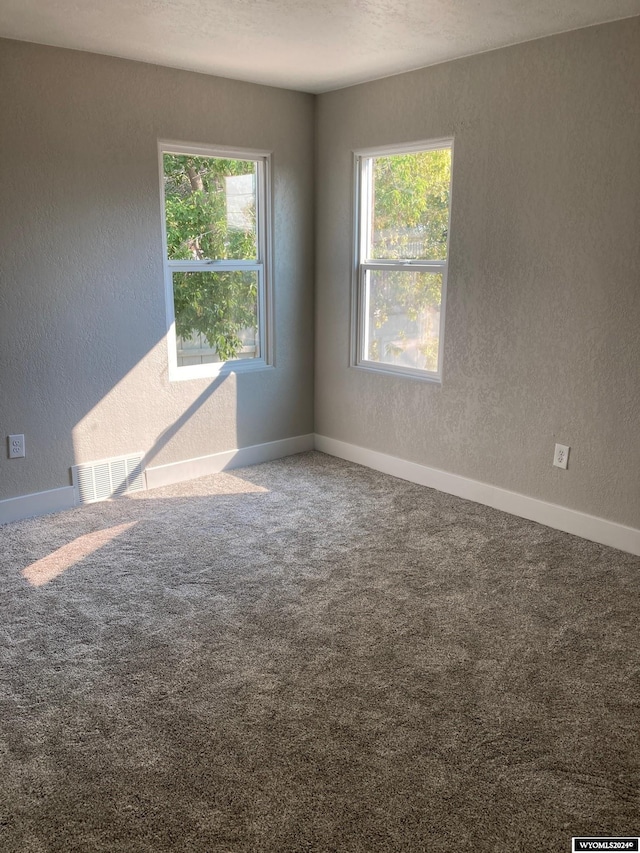 carpeted empty room with a textured wall, baseboards, and visible vents