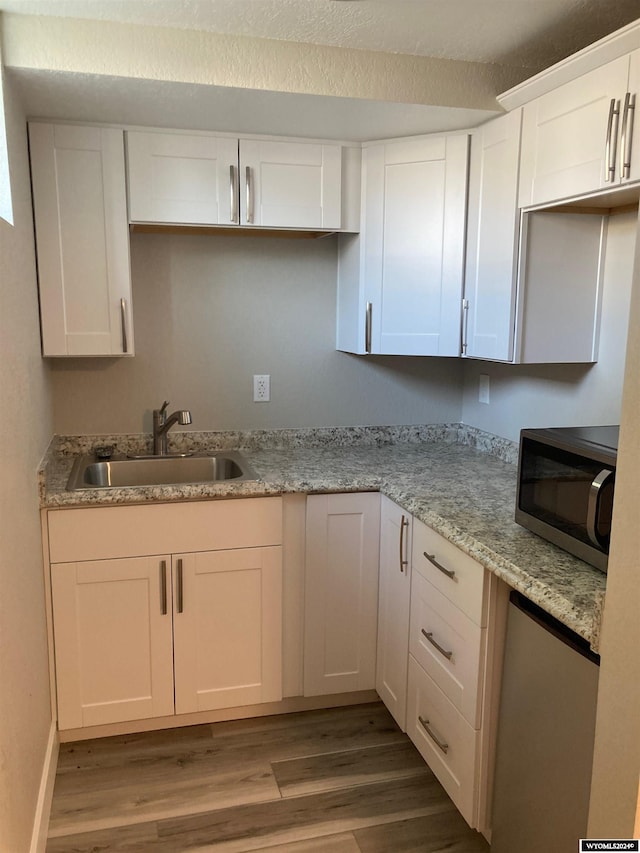 kitchen featuring white cabinets, wood finished floors, a sink, and stainless steel microwave