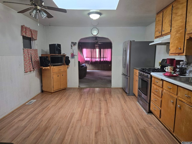 kitchen featuring light wood-type flooring, ceiling fan, appliances with stainless steel finishes, and tile walls