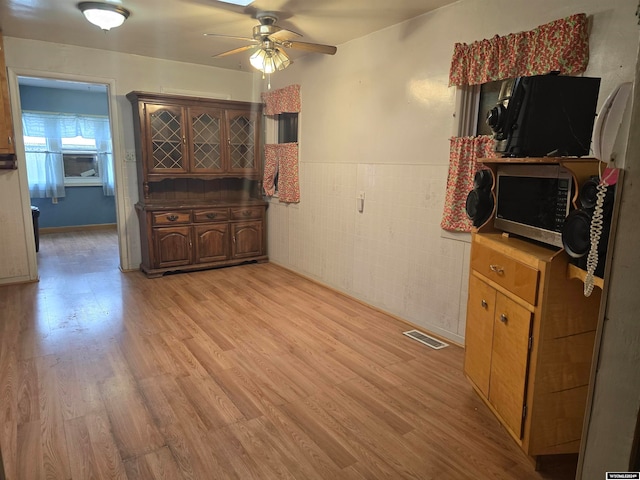 interior space with tile walls, light wood-style flooring, a ceiling fan, and visible vents