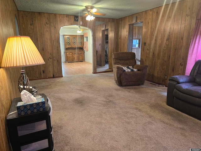 carpeted living room with arched walkways, wood walls, a textured ceiling, and ceiling fan