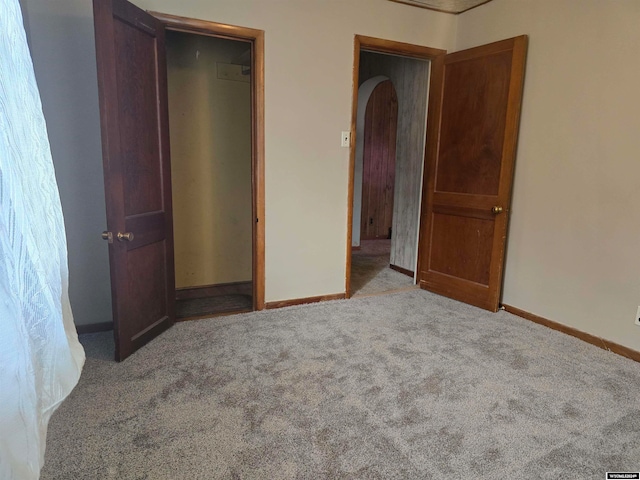 unfurnished bedroom featuring carpet, arched walkways, and baseboards