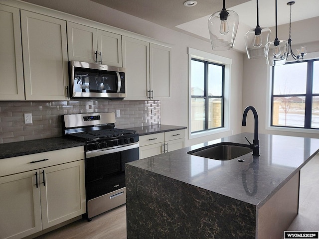 kitchen with appliances with stainless steel finishes, sink, pendant lighting, dark stone counters, and an island with sink