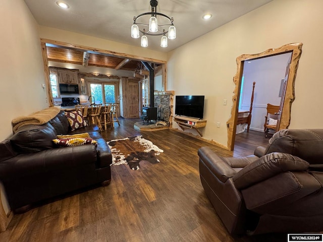 living room featuring a notable chandelier, a wood stove, beam ceiling, and dark wood-type flooring