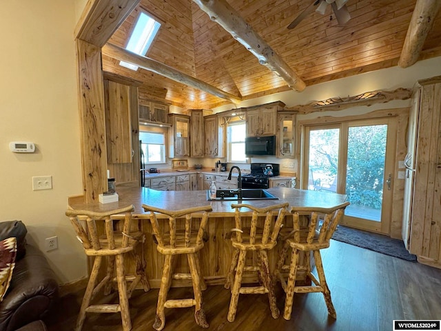 kitchen with sink, kitchen peninsula, dark wood-type flooring, black appliances, and lofted ceiling with skylight