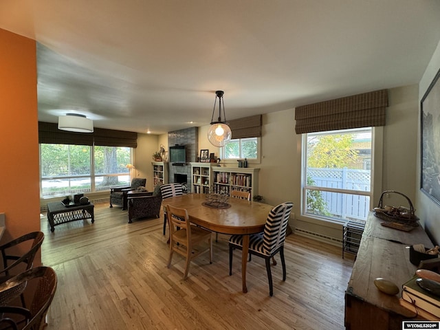 dining space featuring a baseboard radiator, a large fireplace, and light hardwood / wood-style floors