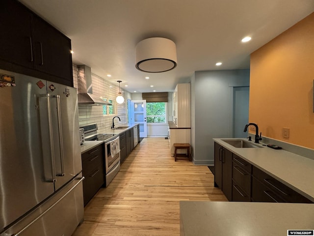 kitchen with pendant lighting, appliances with stainless steel finishes, wall chimney exhaust hood, and sink