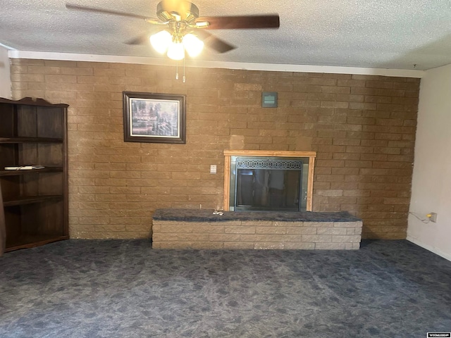 unfurnished living room with ceiling fan, brick wall, a brick fireplace, a textured ceiling, and dark colored carpet